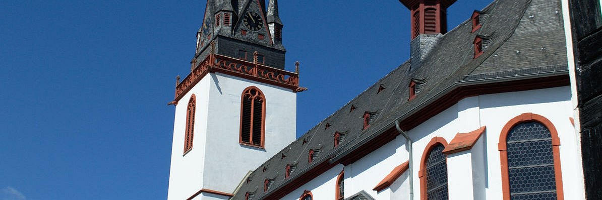 Die Kirche in Erbach mit weißer Fassade, roten Details und schwarz-grauem Schieferdach in der Grundform einer Basilika mit hohem Glockenturm